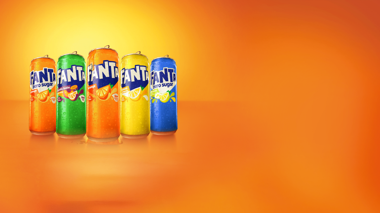 Vijf Fanta‑blikjes in verschillende kleuren en smaken staan naast elkaar aan de linkerkant, tegen een heldere oranje‑gele achtergrond met veel lege ruimte rechts.