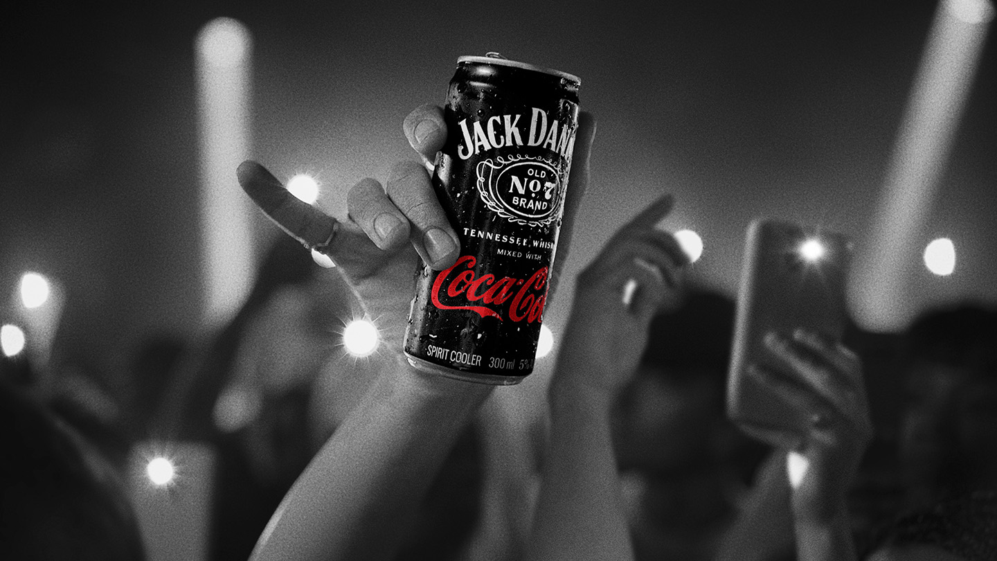 Mão segurando uma lata de Coca-Cola Jack Daniels no meio de uma multidão