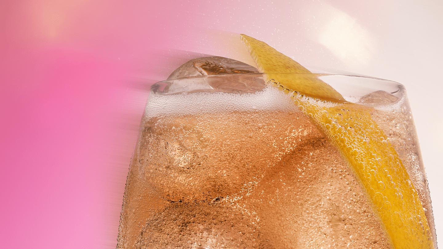 Um Fizzy Peach gelado, decorado com uma rodela de limão, em um close irresistível sobre um fundo rosa vibrante.