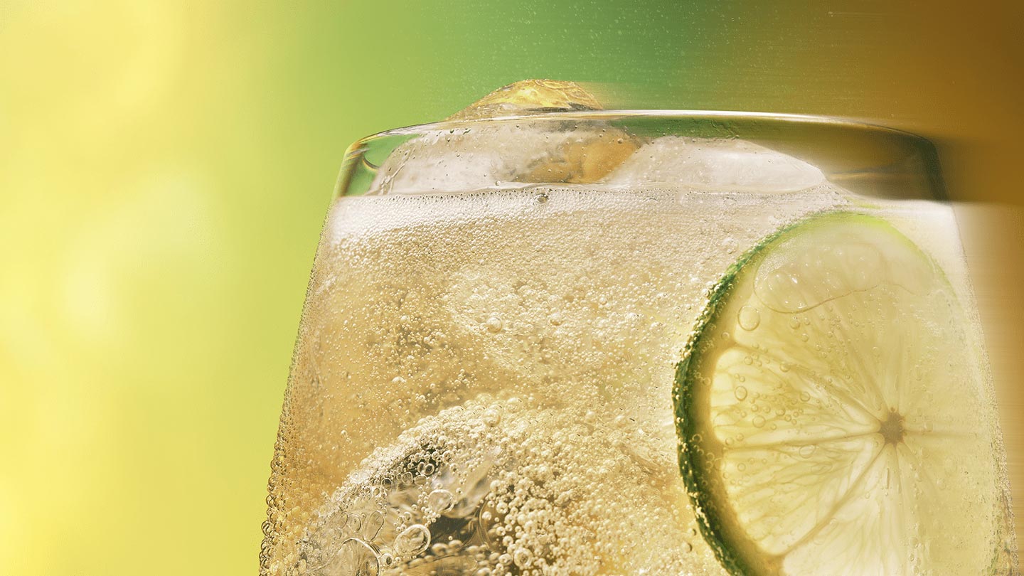 Um Toreador Ginger Ale com cubos de gelo e uma fatia de lima e limão em um copo. A bebida é borbulhante e parece refrescante sobre um fundo verde.