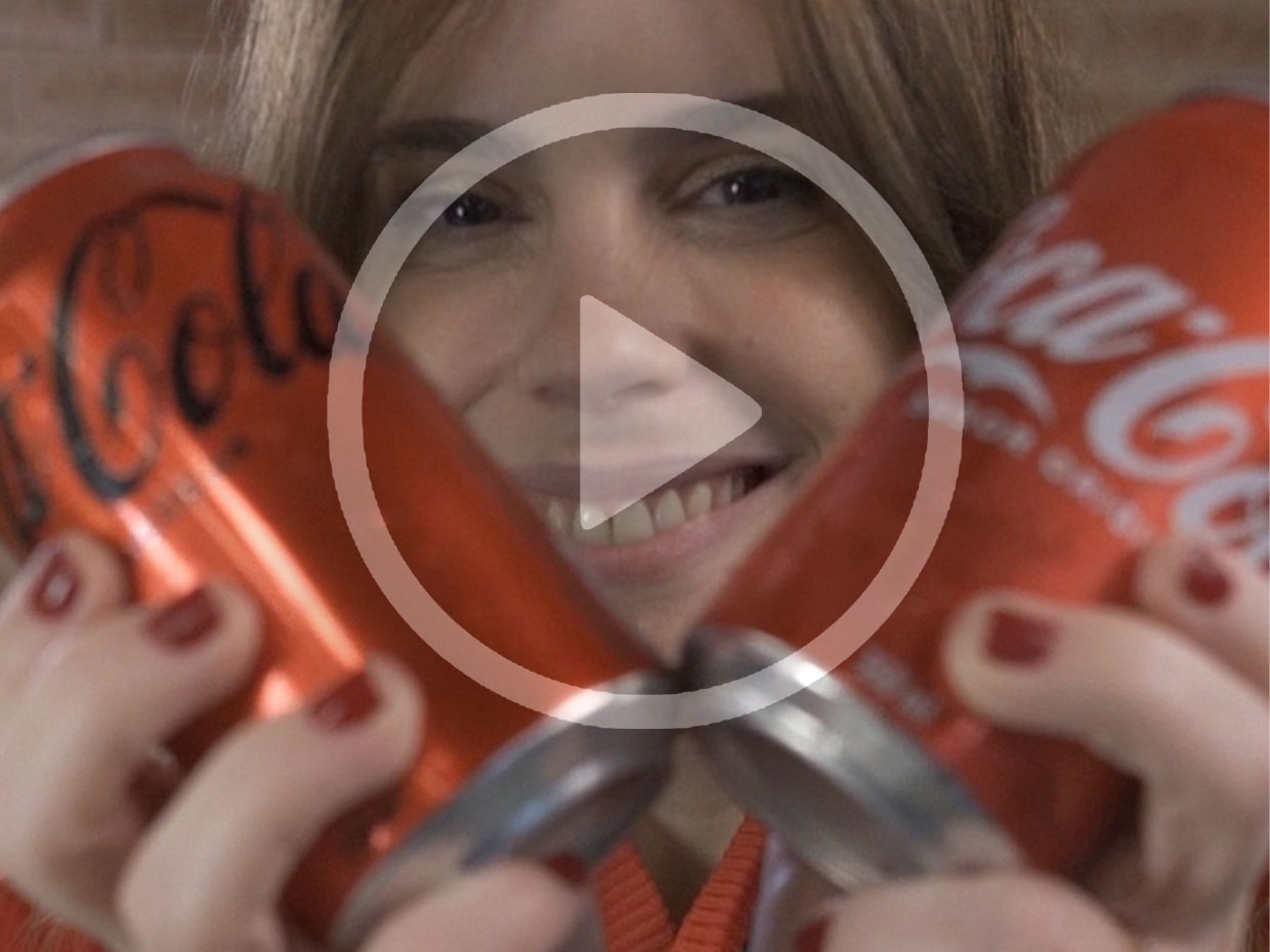 Menina sorrindo, segurando uma lata de Coca-Cola Zero e um sabor original