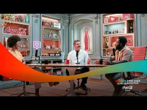 Três pessoas em um estúdio de podcast, com prateleiras cheias de itens da Coca-Cola ao fundo.