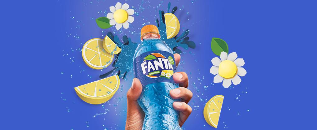 eine Hand, die eine Fanta Shokata Flasche hochhält, umgeben von Blumen und Zitronenschnitzen