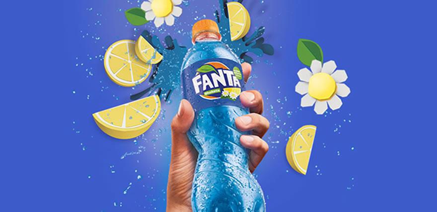 eine Hand, die eine Fanta Shokata Flasche hochhält, umgeben von Blumen und Zitronenschnitzen