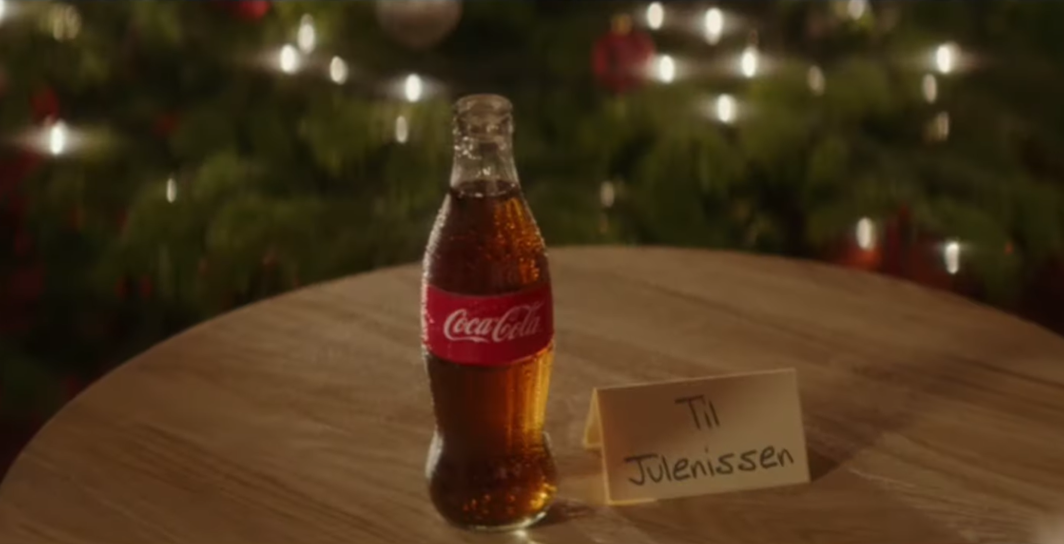 Eine Coca-Cola Flasche auf einem Tisch mit einem Weihnachtsbaum im Hintergrund