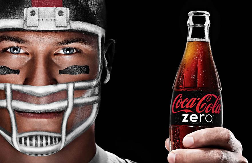 Homme avec un casque de rugby peint tenant une bouteille de Coca-Cola Zero sans sucre dans la main, sur fond noir.
