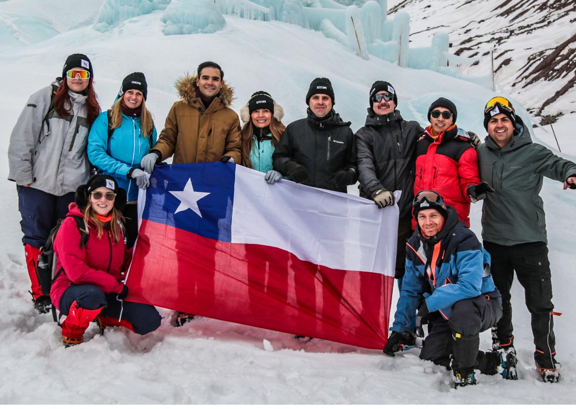 Grupo de amigos con bandera chilena en la nieve, celebrando la aventura en la cordillera