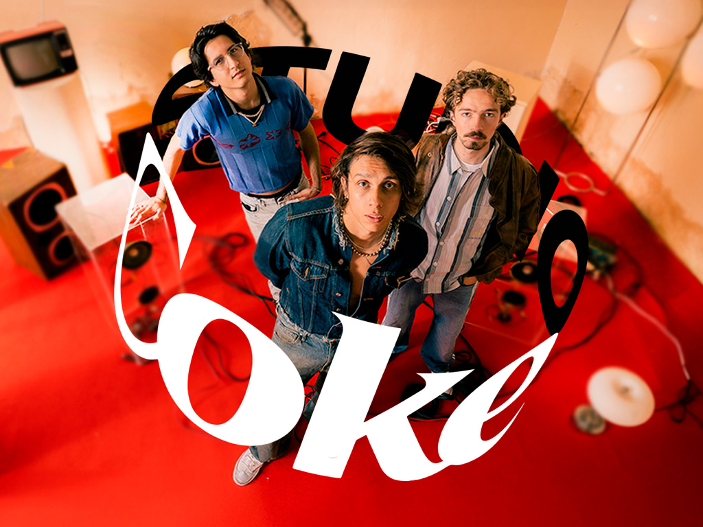 La banda Timo en un estudio con piso rojo miran a la cámara en picado; equipos de audio al fondo y logo curvo de “Coke Studio” superpuesto.