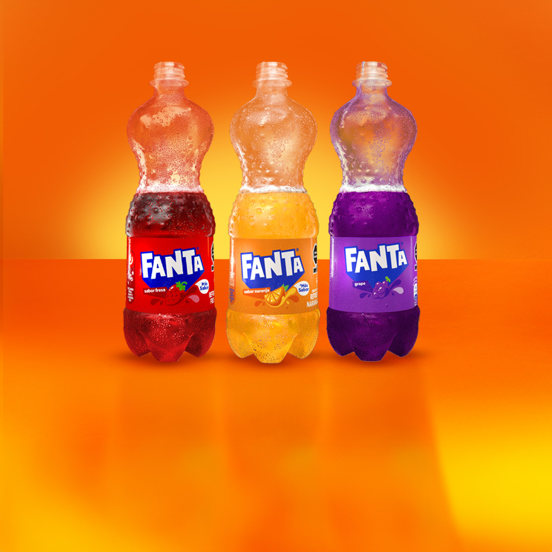 Tres botellas de Fanta de diferentes sabores - fresa, naranja y uva - destapadas con el refresco por la mitad, alineadas sobre fondo naranja brillante.