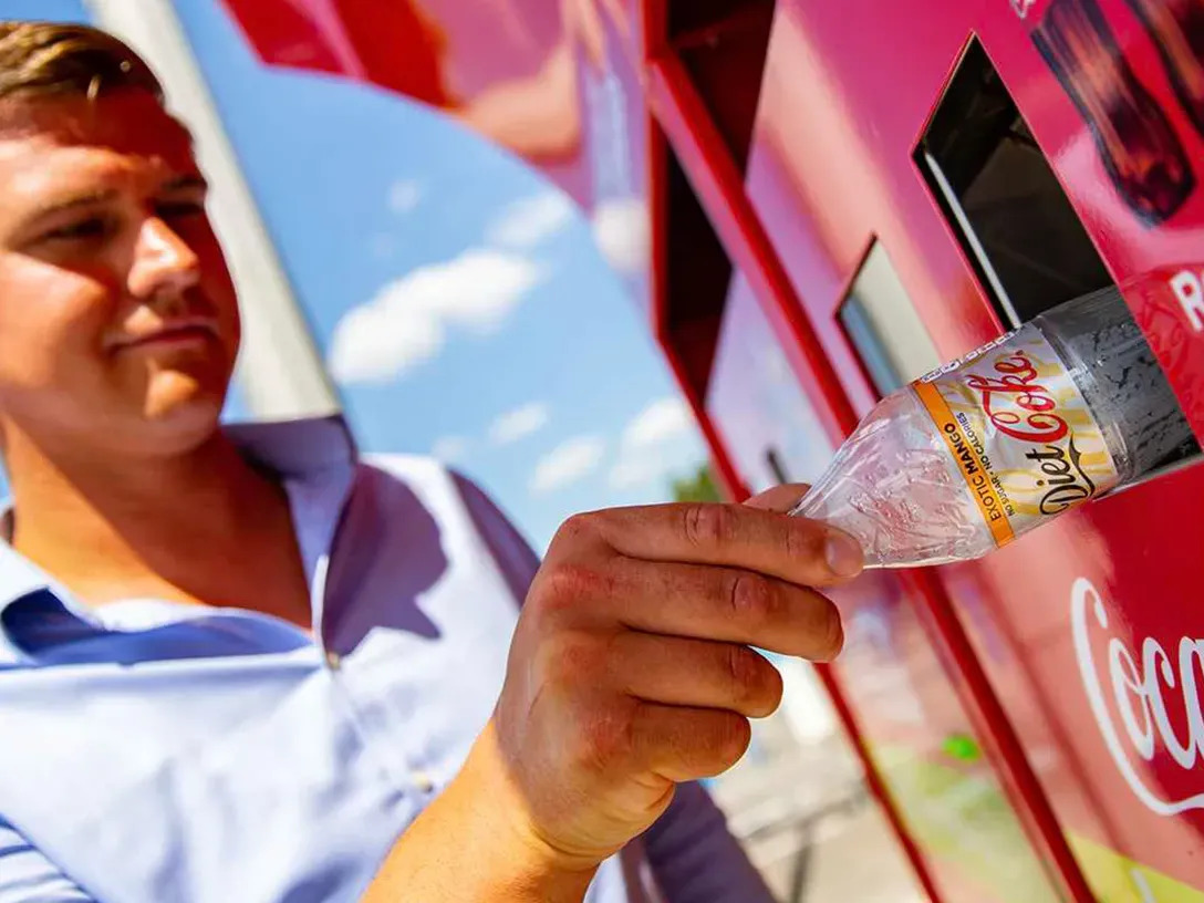 Un homme jette une bouteille de Coca-Cola usagée dans une poubelle de recyclage