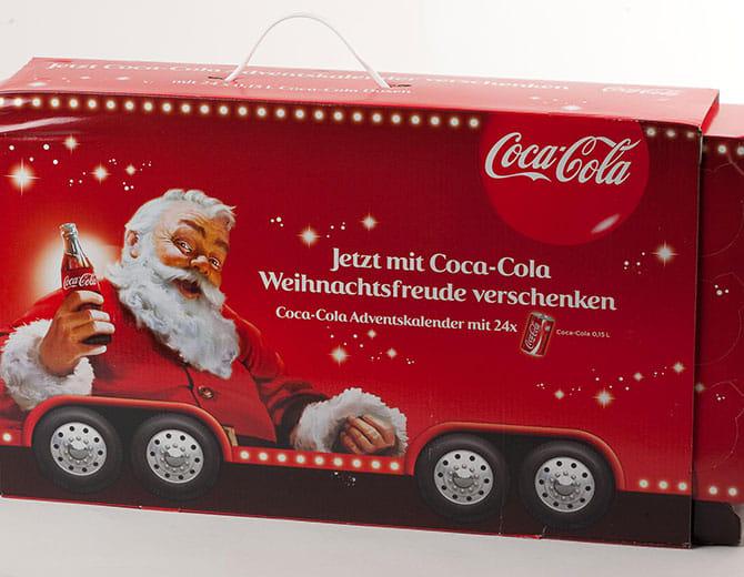 Punane Coca‑Cola advendikalendri karp jõuluvana ja Coca‑Cola pudeliga, kaunistatud tulede ja lumehelvestega.