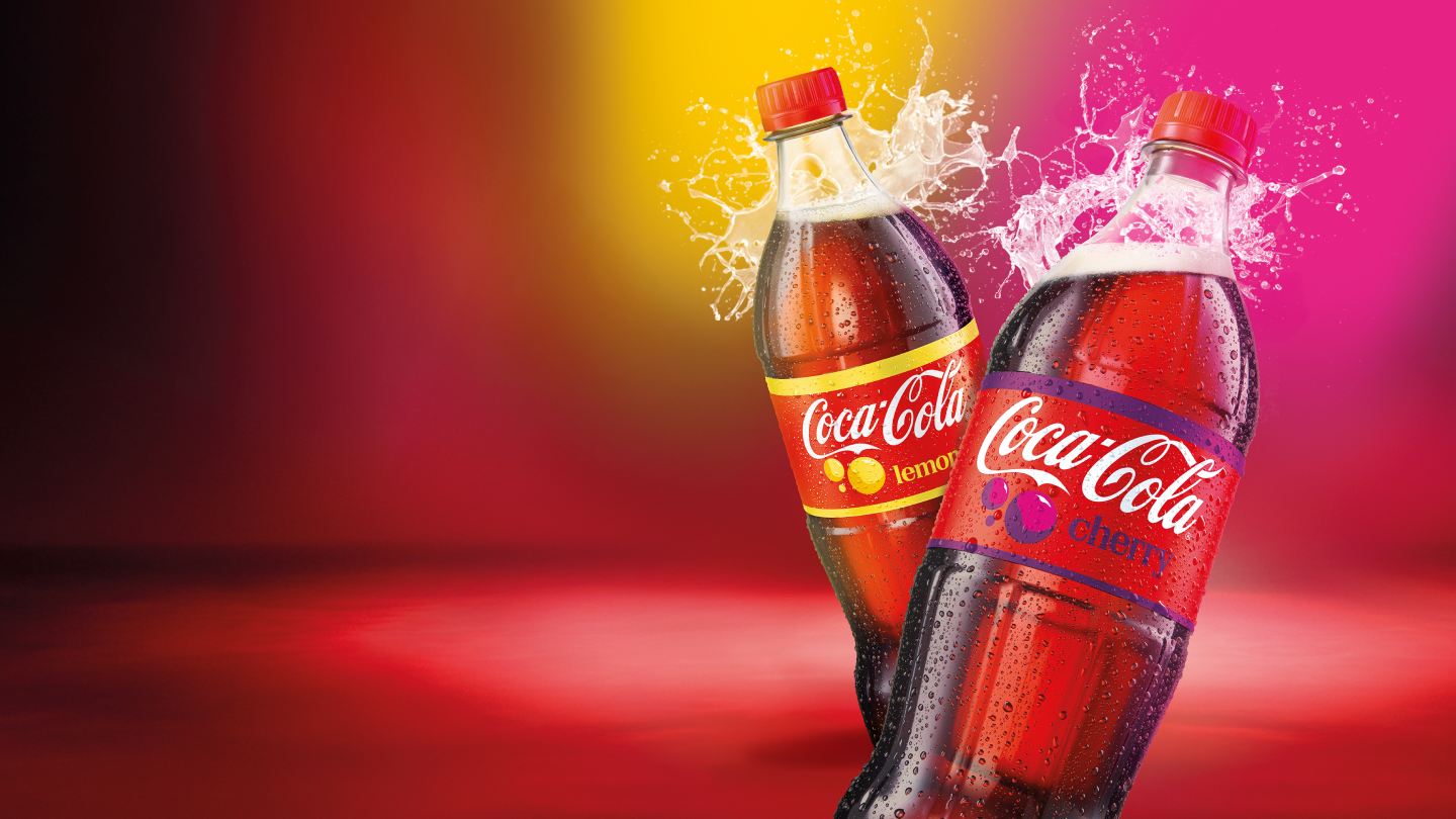 Kaks Coca‑Cola pudelit, sidruni- ja kirsimaitseline, värvilisel taustal pritsiva joogiga.