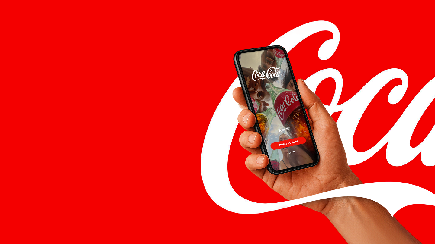 Ruka drží chytrý telefon s aplikací Coca‑Cola na červeném pozadí.