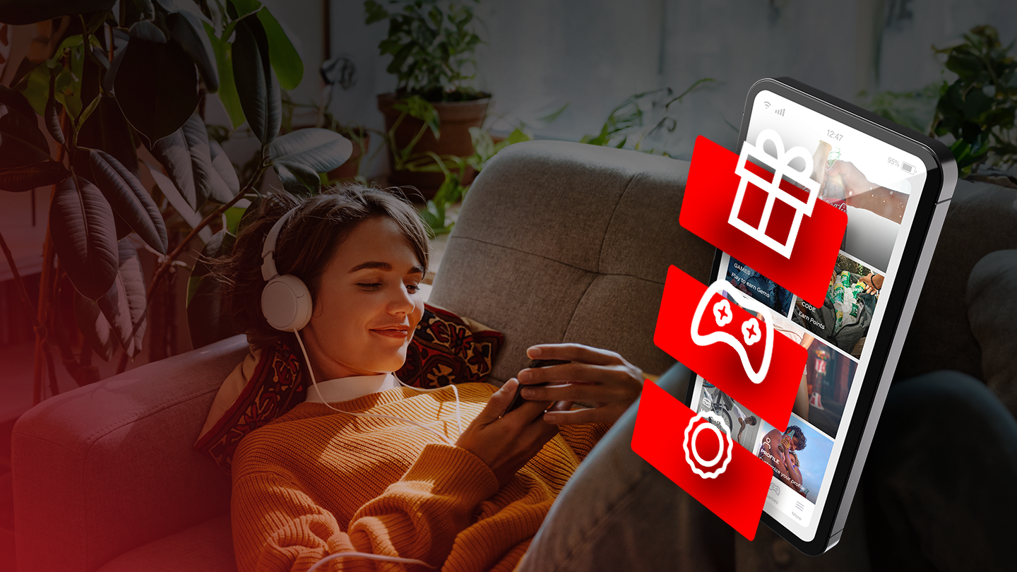 Osoba koristi mobilni telefon sa Coca-Cola aplikacijom i crvenim ikonicama poklona, gejming kontrolera i bedža, uz promotivni tekst