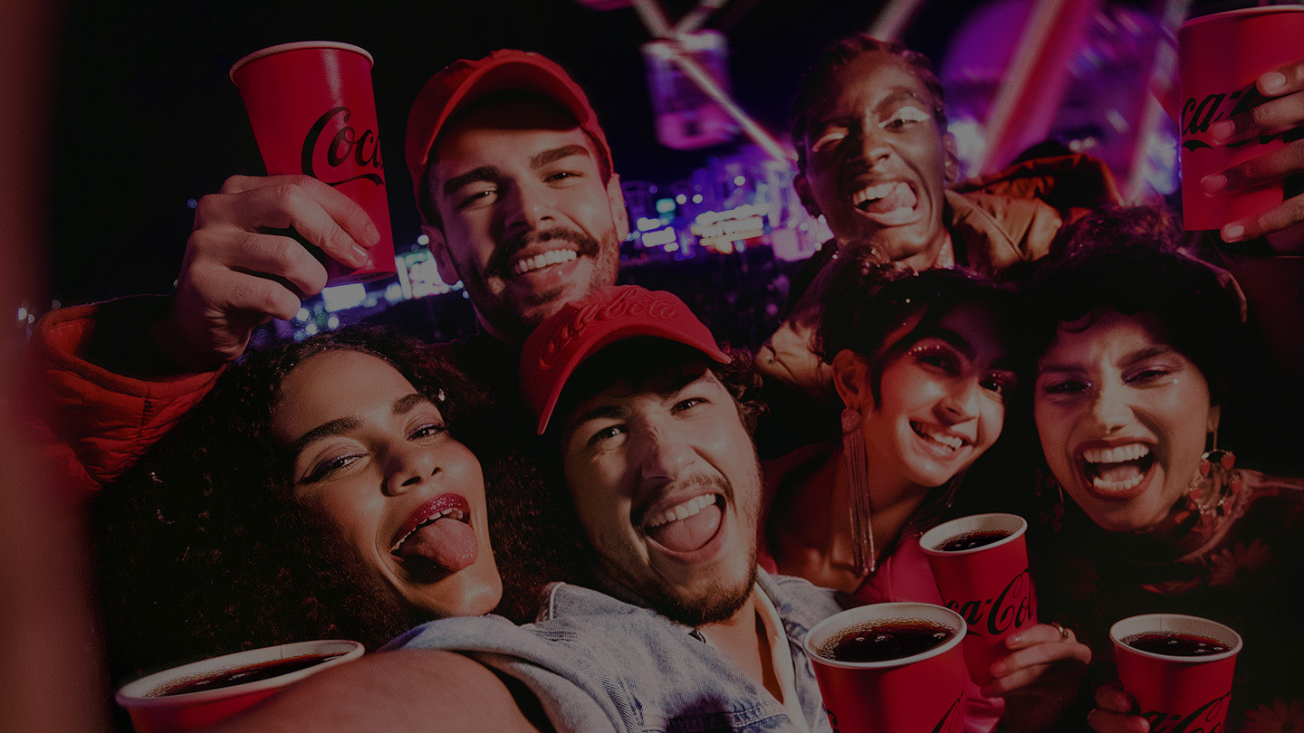 Grupo de amigos disfrutando de un evento nocturno con vasos rojos de Coca-Cola, sonrientes y rodeados de luces festivas.