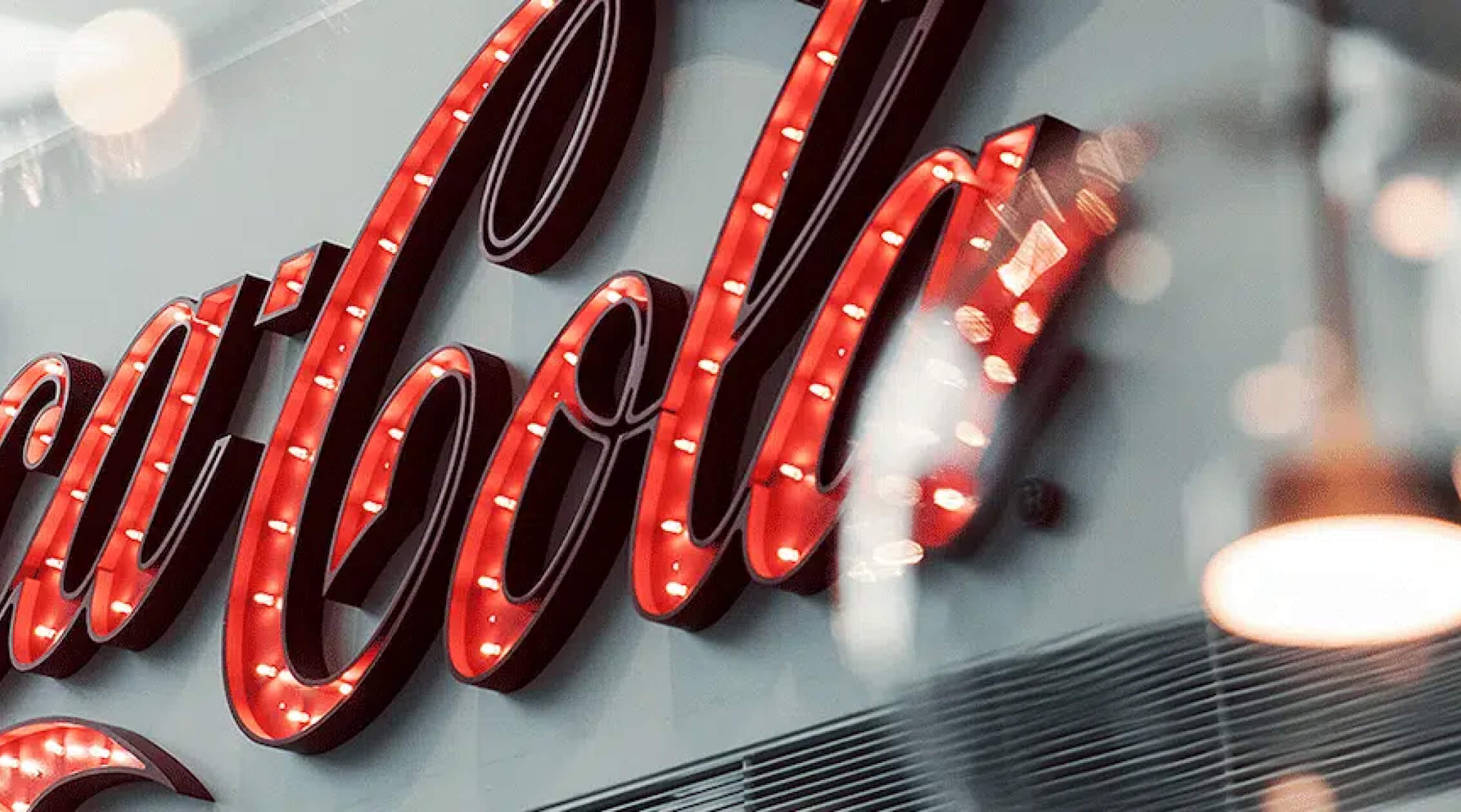 Foto met een groot rood verlicht Coca‑Cola logo aan een binnenmuur.