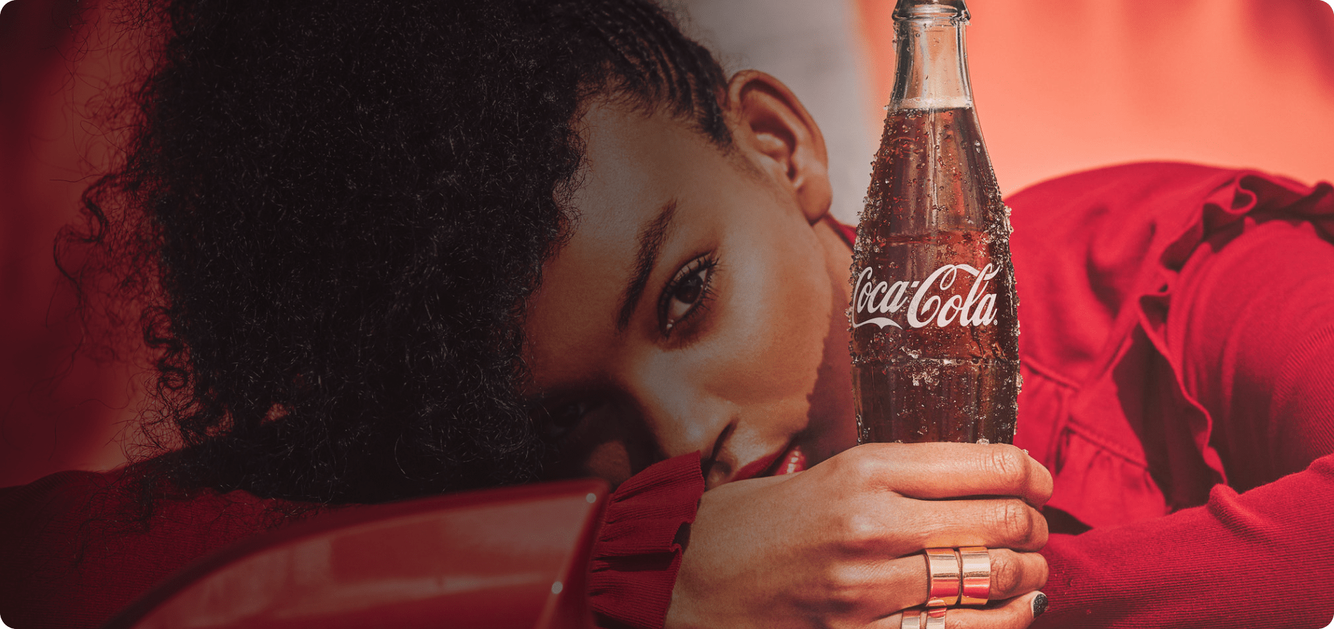 Osoba obučena u crvenu odeću drži staklenu bocu Coca-Cole sa kapljicama kondenzacije.