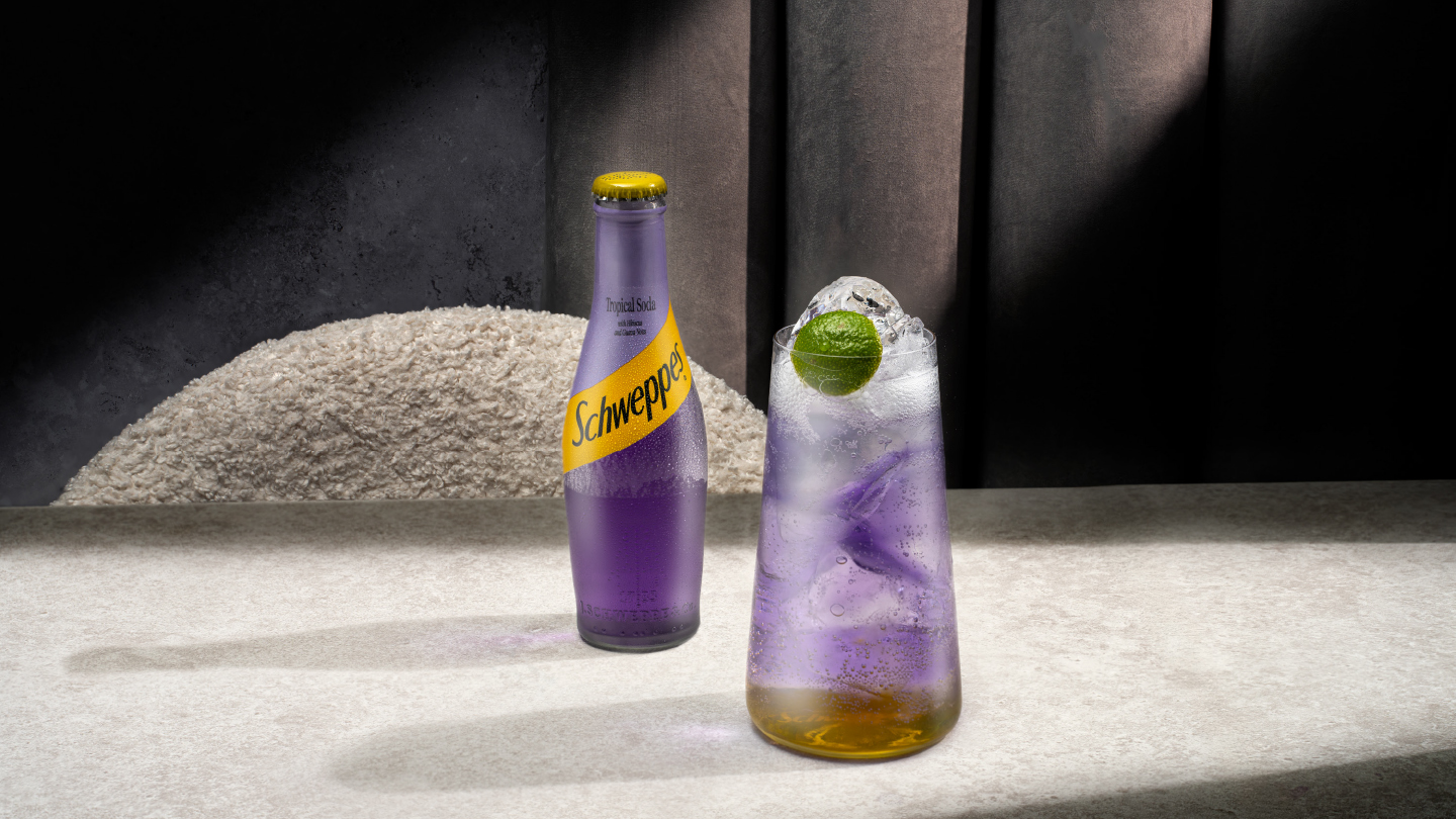schweppes tropical soda bottle and a glass of tropical margarita on a table