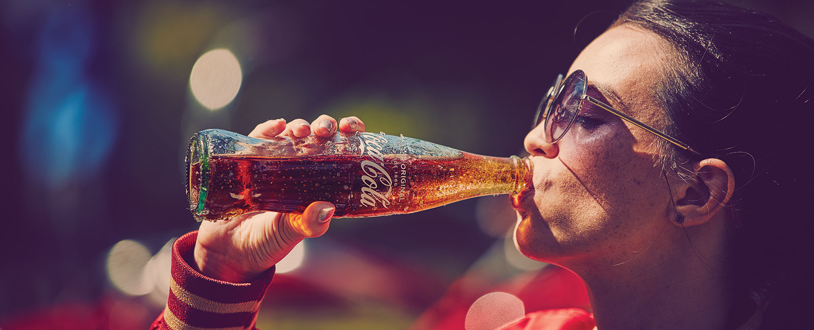 Dorë mban një shishe qelqi Coca-Cola të pjerrët me pika kondensimi në dritën e diellit.