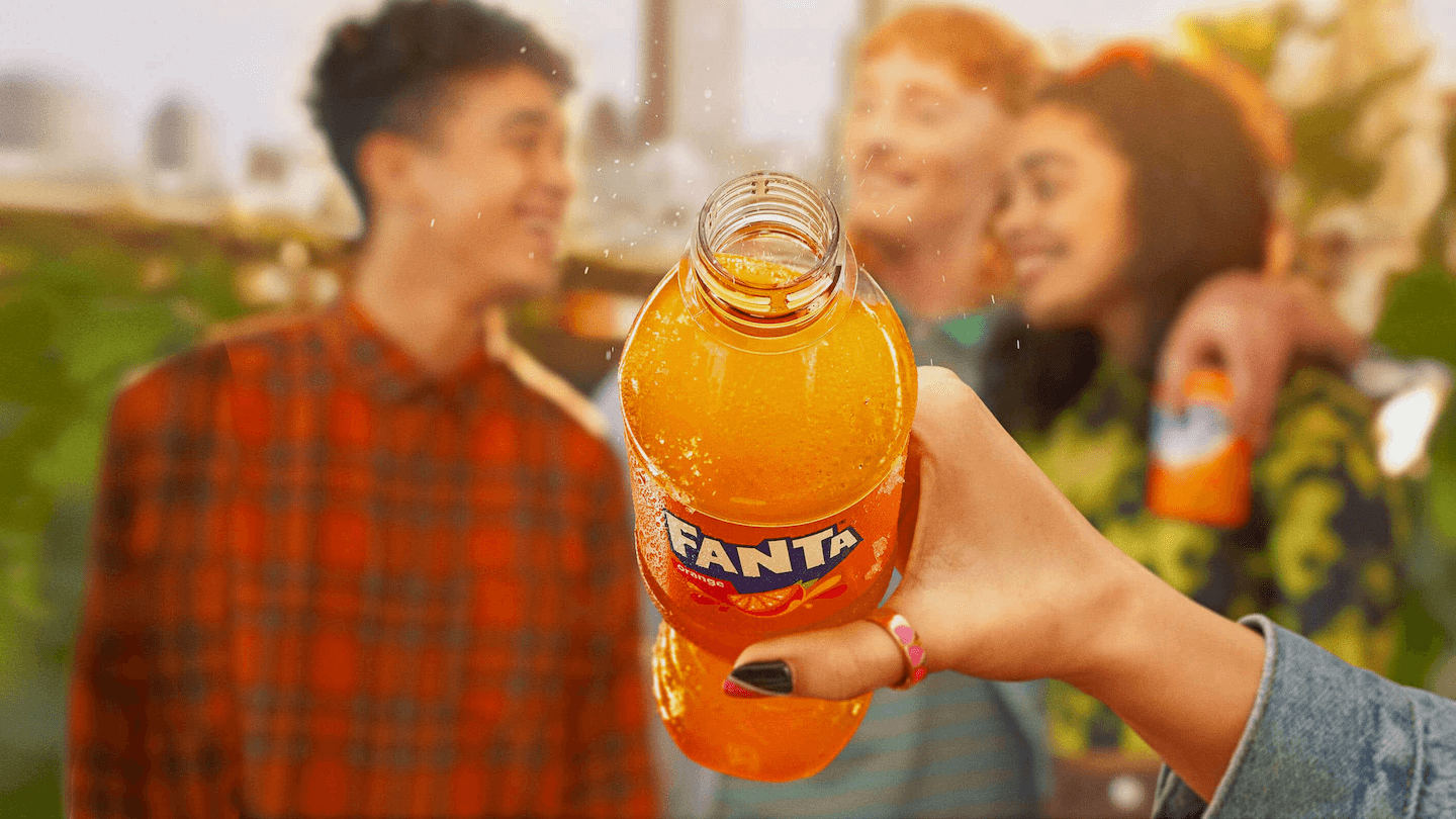 Dorë mban një shishe të hapur Fanta Orange me pika kondensimi.