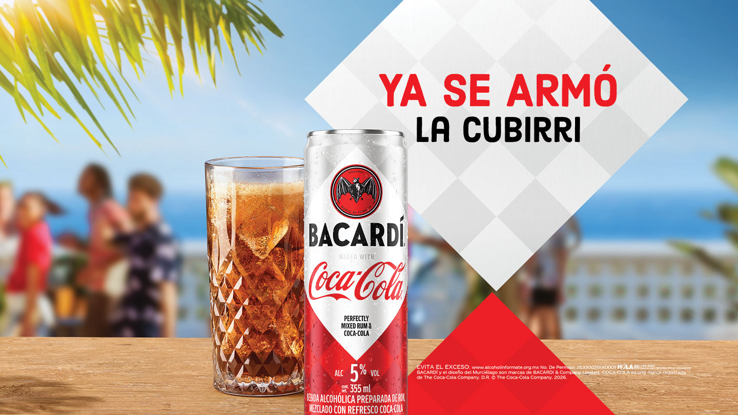 Bacardi y Coca-Cola enlatados y un vaso con bebida en un ambiente playero, con el texto "YA SE ARMÓ LA CUBIRRI".