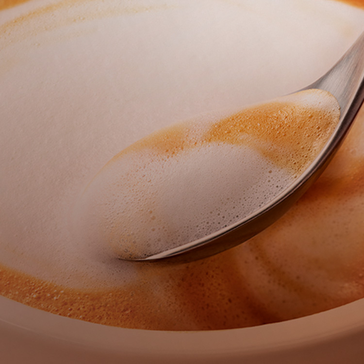 Cuchara introduciéndose en una taza espumosa de café Costa Coffee.