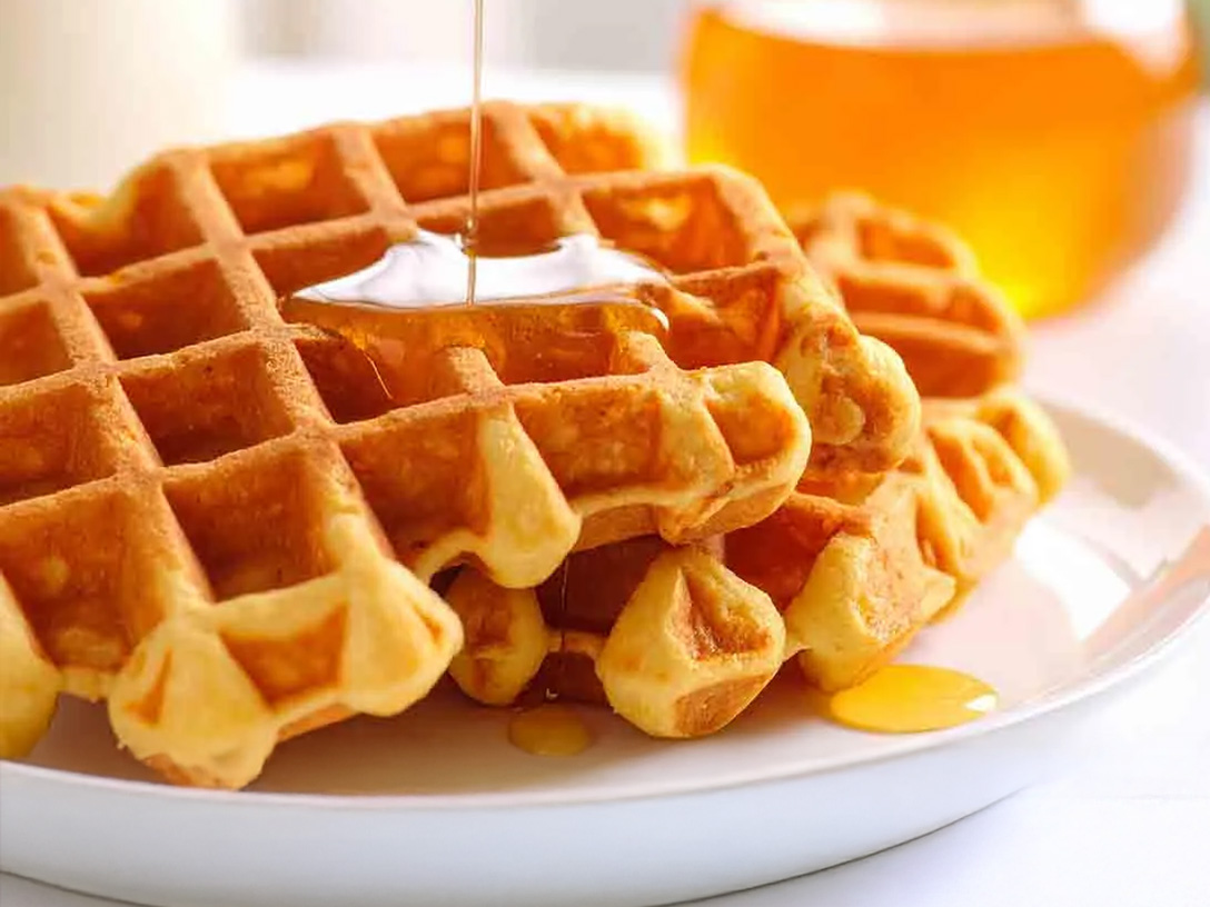Waffles dorados con miel en un plato blanco. Abajo, una franja borgoña con el texto "WAFFLES" y el logo de Santa Clara, indicando "PREPARADOS CON LECHE SANTA CLARA".