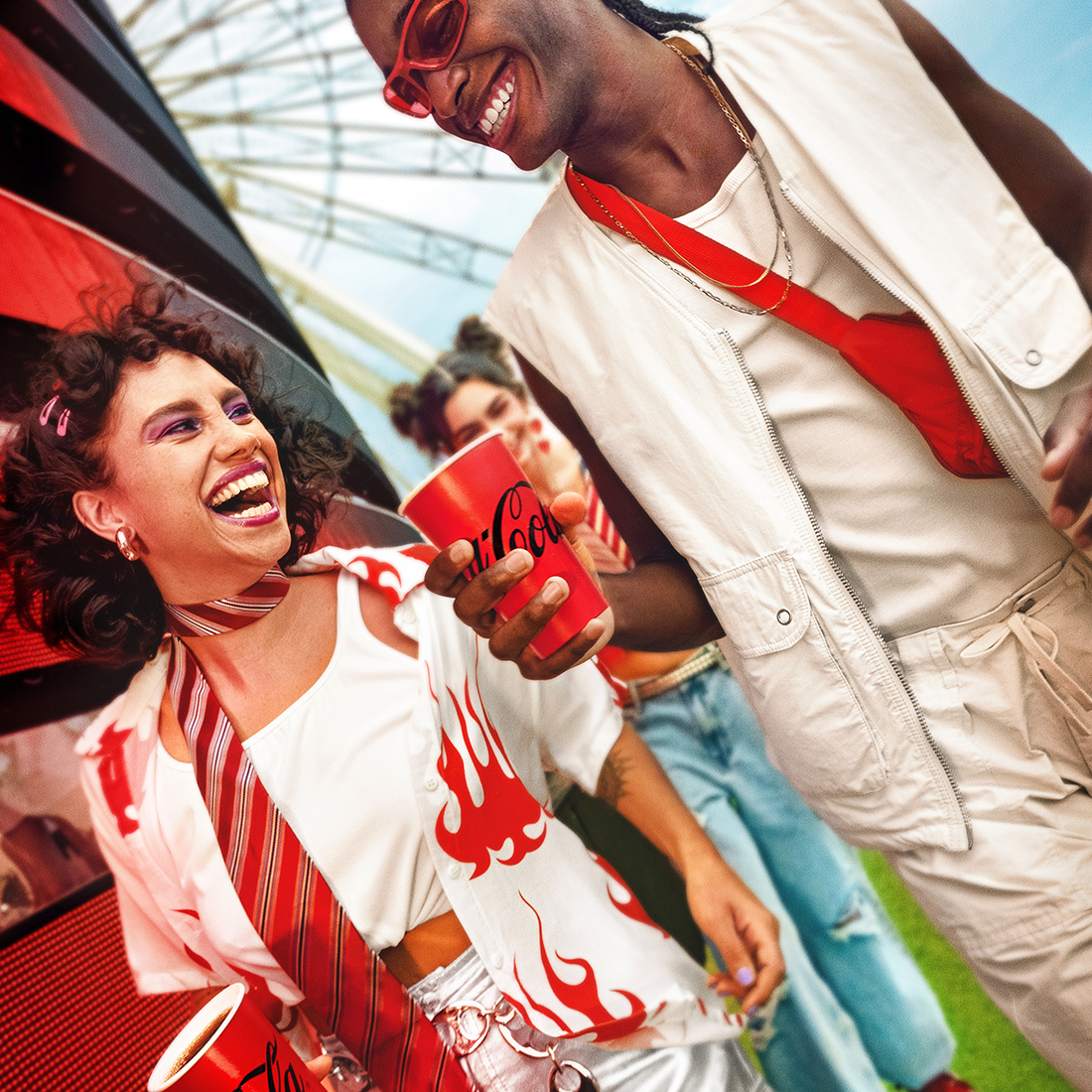 Dos personas riendo y disfrutando de Coca-Cola en un evento al aire libre.