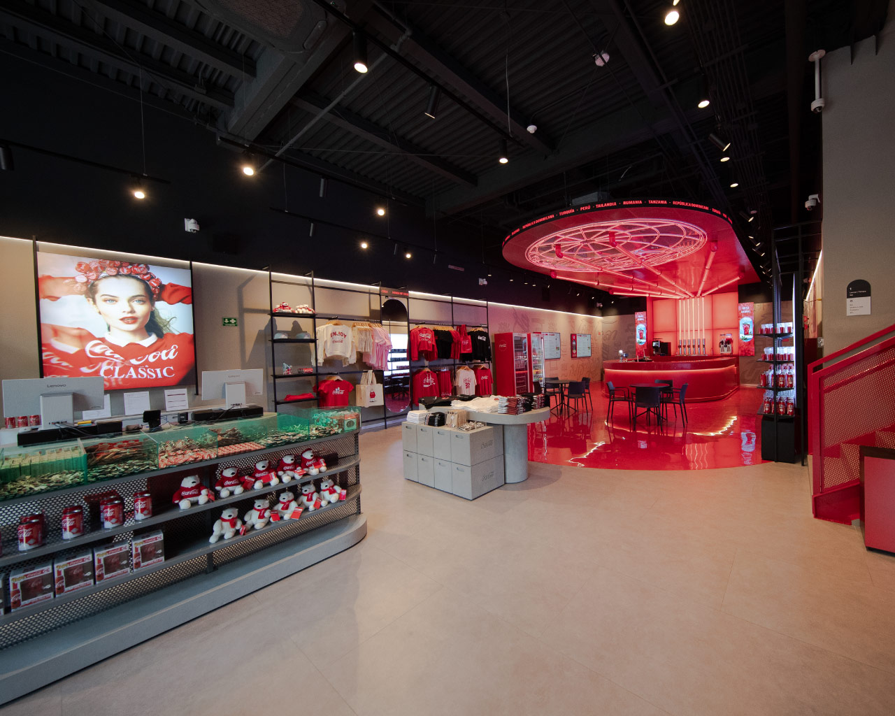 Interior de House of Coca-Cola con barra central, mesas para visitantes, iluminación roja y exhibición de productos de la marca.