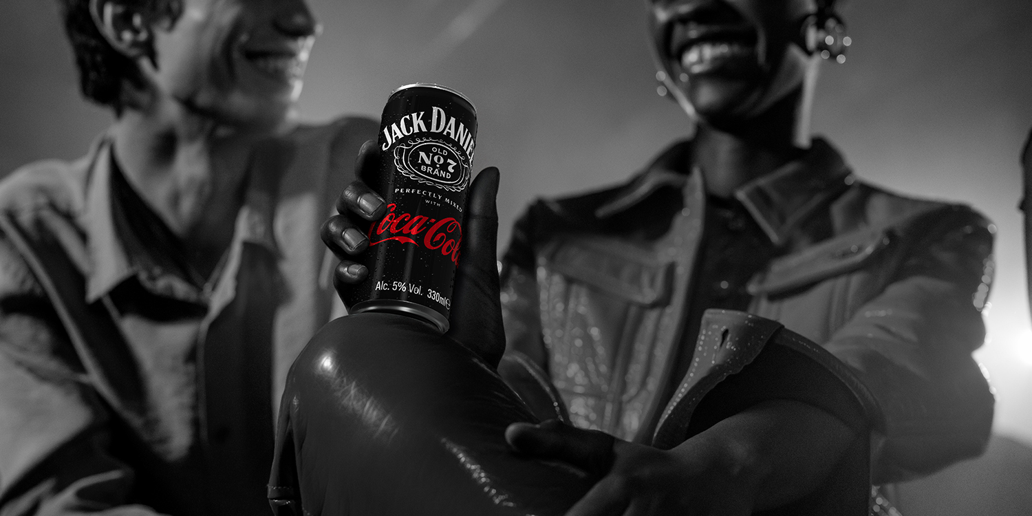Image d'une personne vêtue d'un pantalon clair, une main tenant une canette noire avec le logo Jack Daniel's et Coca-Cola. L'accent est mis sur la canette.