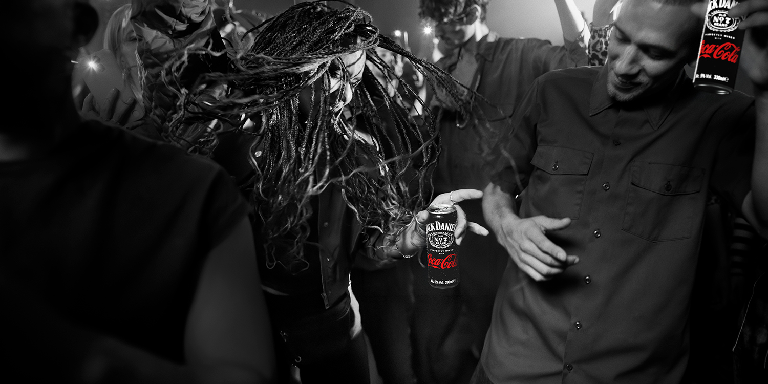 Un groupe d’amis danse et fait la fête lors d’une soirée. Une canette Jack Daniel’s & Coca‑Cola est tenue au premier plan. L’image est majoritairement en noir et blanc, avec la canette mise en évidence, et un encart de texte évoquant le partage et les moments spontanés.