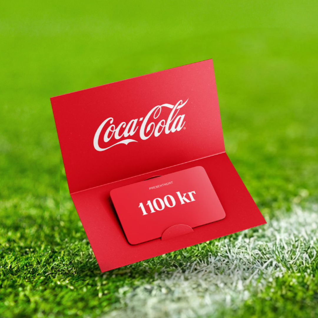 Ett rött Coca‑Cola‑presentkort på 1 100 kronor ligger i ett öppnat rött omslag med Coca‑Cola‑logotypen, placerat på grönt gräs som liknar en fotbollsplan.