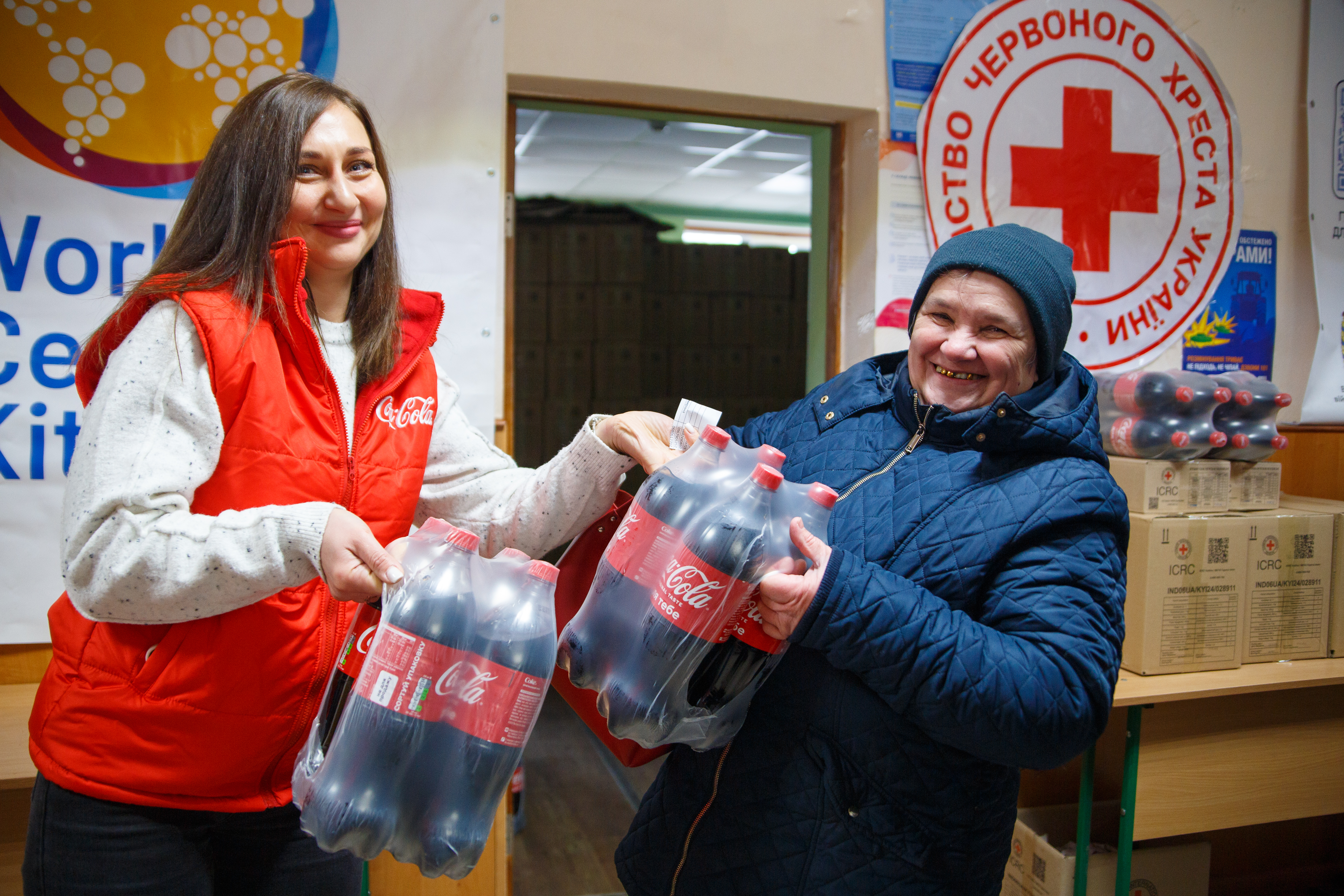 Волонтер передає упаковки напою Coca‑Cola 