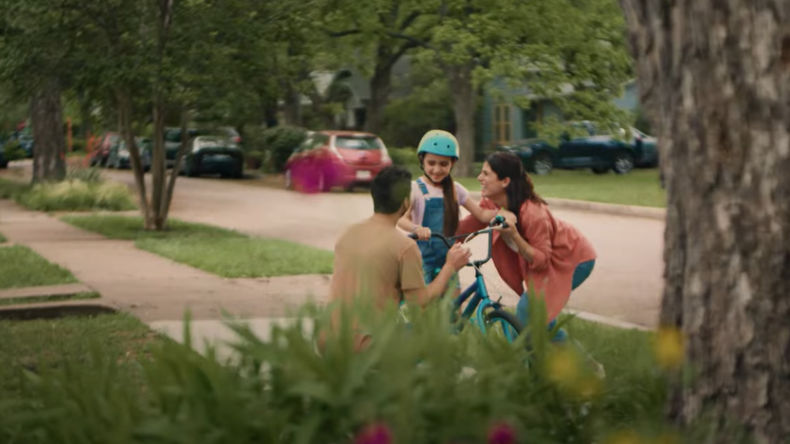 A mother and father teach their child how to ride a bike.