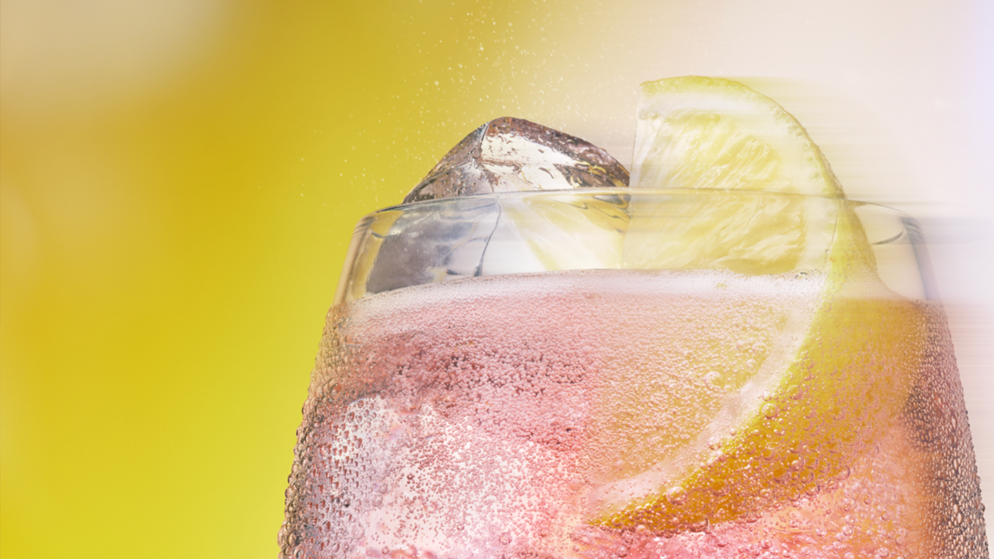 Un Toreador Ginger Ale con cubitos de hielo y una rodaja de lima y limón en un vaso. La bebida está burbujeante y parece refrescante sobre un fondo verde.